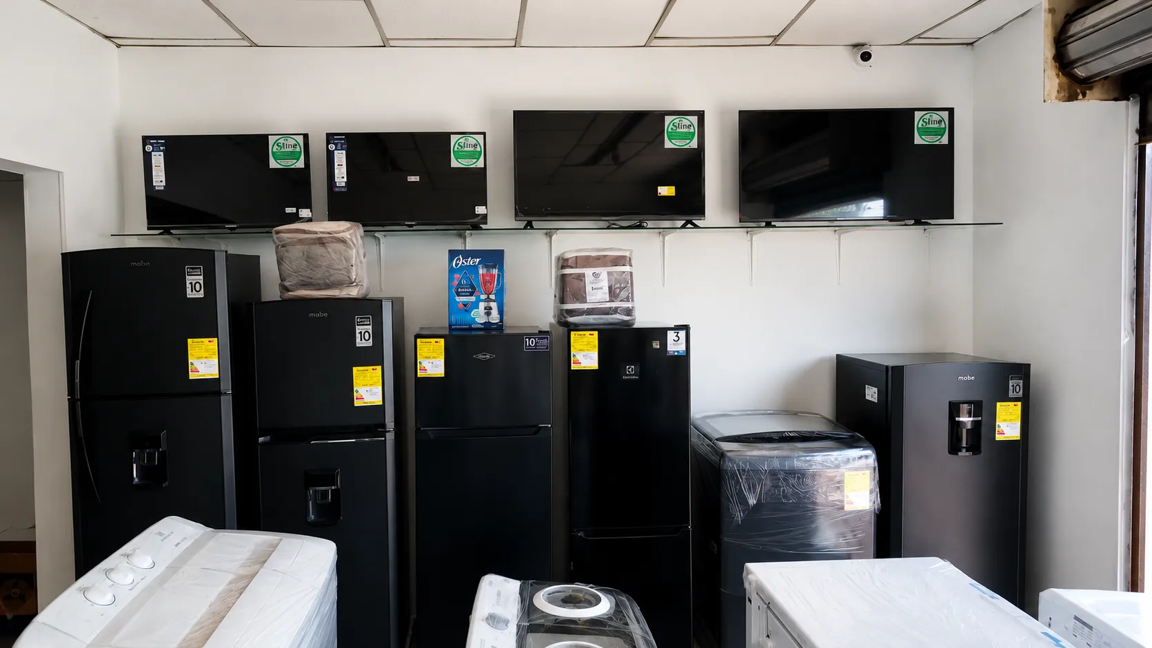 Interior del almacén Bahía: neveras Mabe y Electrolux alineadas bajo una repisa con televisores, con lavadoras y una licuadora Oster.